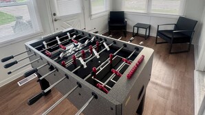 A room with a foosball table, a door, and windows with blinds.