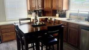 A modern kitchen with wooden cabinets, a dining table with chairs, a ceiling fan, and a window with blinds.