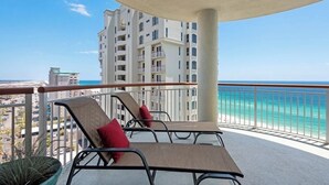 Un balcón con dos sillones de descanso y una mesa, con vistas a una playa y un edificio de gran altura.