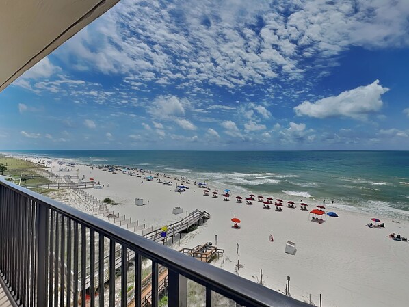 A beach with umbrellas and people, a pier, and a clear sky.