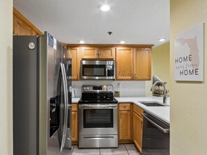 A modern kitchen with stainless steel appliances, wooden cabinets, and a white countertop.
