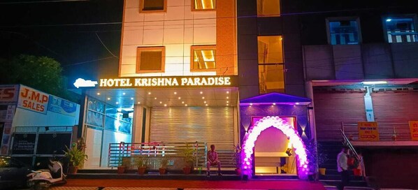 Exterior del Hotel Krishna Paradise, con entrada cerrada y un arco luminoso.