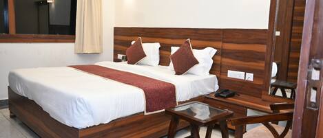 A hotel room with a wooden bed, white bedding, a red throw blanket, a bedside table with a phone, and a mirror.