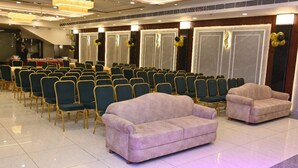 A conference room with rows of chairs, a stage, and two sofas. - HOTEL KRISHNA PARADISE (Agra)