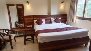 A bedroom with a large bed, a wooden desk, a chair, a mirror, and two wall-mounted lights. - HOTEL KRISHNA PARADISE (Agra)