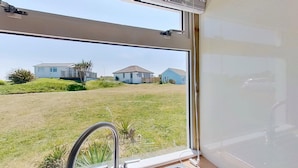 A view from inside a room with a large window overlooking a grassy area with houses.