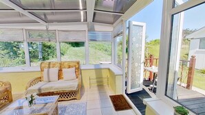 A sunroom with a sofa, a small table, and a view of the garden.
