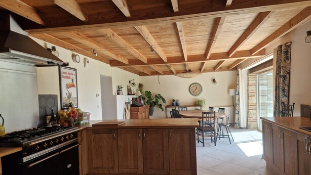 A kitchen with wooden beams, a stove, cabinets, a dining table with chairs, and a hanging light fixture. - Mas Crudel - Character house in the South of France (Parisot)