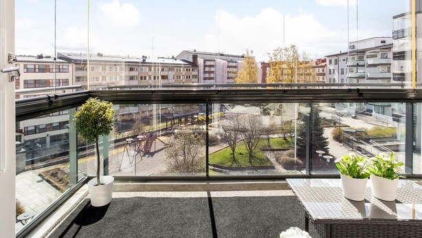 A balcony with a view of a cityscape, a small potted plant, and a wicker chair. - Kotimaailma KotikaksioMallask saunalla (Lahti)