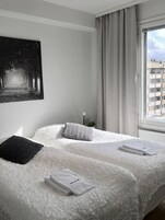 Hotellihuone, jossa on kaksi sänkyä, mustavalkoinen maalaus, ikkuna, jossa on verhot, ja näkymä rakennuksiin.