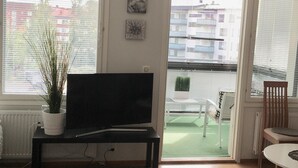 A living room with a TV on a stand, a potted plant, and a view of the outside balcony. - Kotimaailma KotikaksioMallask saunalla (Lahti)