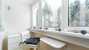 Ein Kinderzimmer mit einem weißen Schreibtisch, einem Stuhl und einem Fenster mit Blick auf Bäume.
