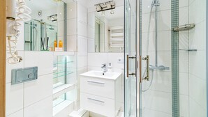Ein modernes Badezimmer mit Duschkabine aus Glas, einem weißen Waschbecken mit Spiegel darüber und einer Glasregaleinheit.