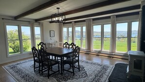 Une salle à manger dotée d’une grande table et de chaises, entourée de larges fenêtres donnant sur un paysage verdoyant.