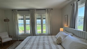 Une chambre avec un grand lit, une chaise, une lampe sur pied et une vue sur un paysage verdoyant par les fenêtres.