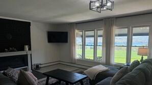 Un salon avec une cheminée, une grande fenêtre donnant sur un lac, un canapé et une table basse.