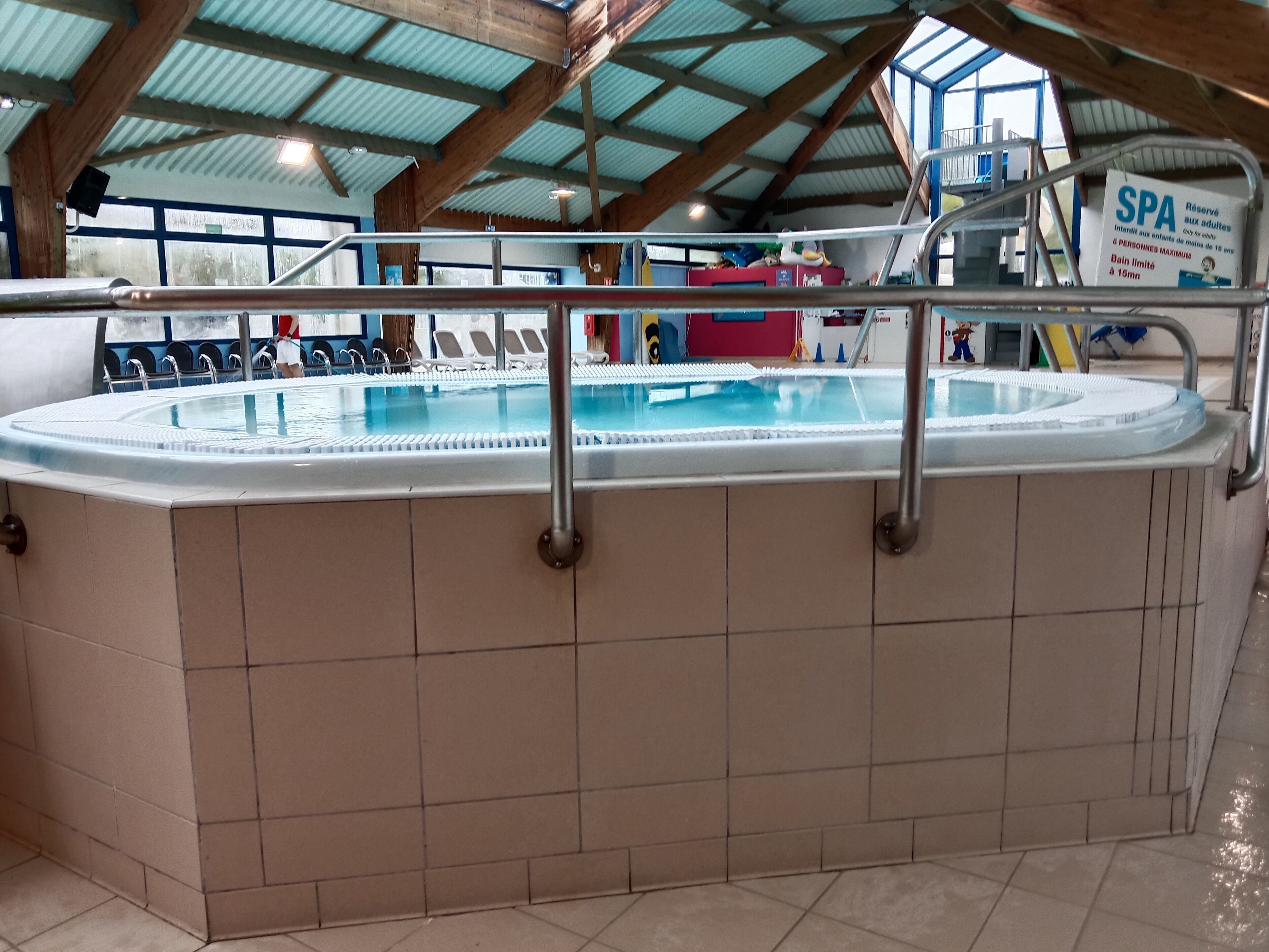 Une piscine avec un sol carrelé et une rambarde en métal.