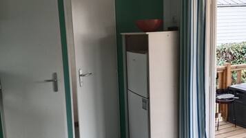 A compact room with a white refrigerator, a door with a green stripe, and a view of a wooden deck outside.