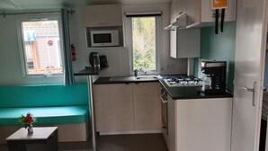 Cocina funcional con microondas, estufa y lavamanos. Incluye un banco color turquesa y una mesa pequeña con un jarrón.