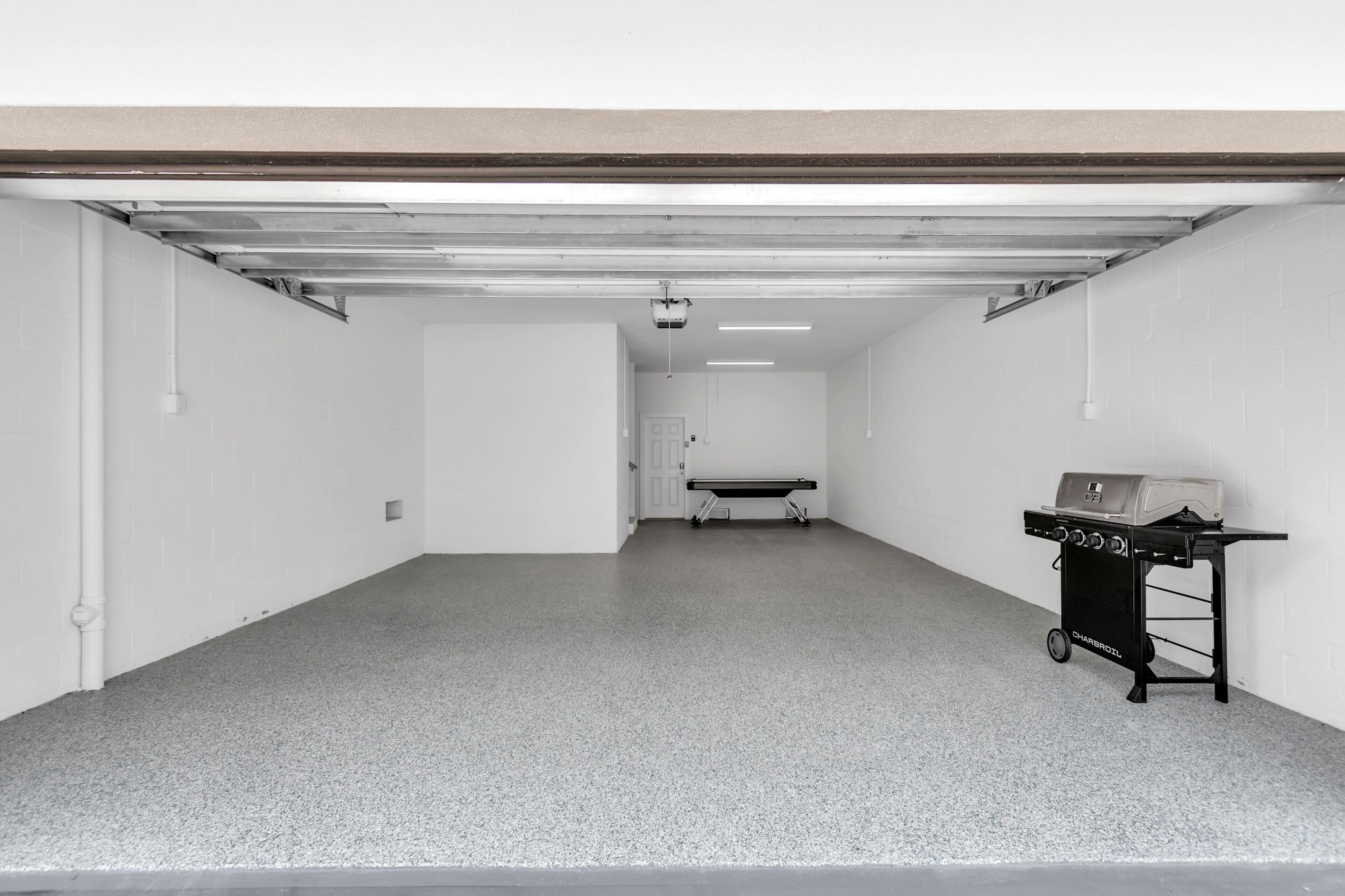 A garage with a concrete floor, a ceiling with exposed beams, and a black grill cart.