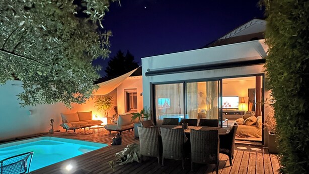 Een modern terras buiten met een zwembad, een zitgedeelte en een glazen ruimte.