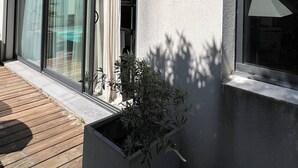 Een modern gebouw met grote schuifdeuren, een houten terras en een plant in een pot.