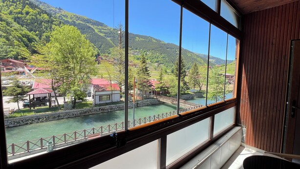 Vista desde una habitación con ventanas amplias que dan al río, un puente y un paisaje montañoso.