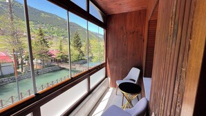 Un balcón con vista a un río y montañas, una silla y una mesita.
