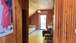 Un interior de madera con un sofá y una silla, un cuadro en la pared y una ventana con vistas.