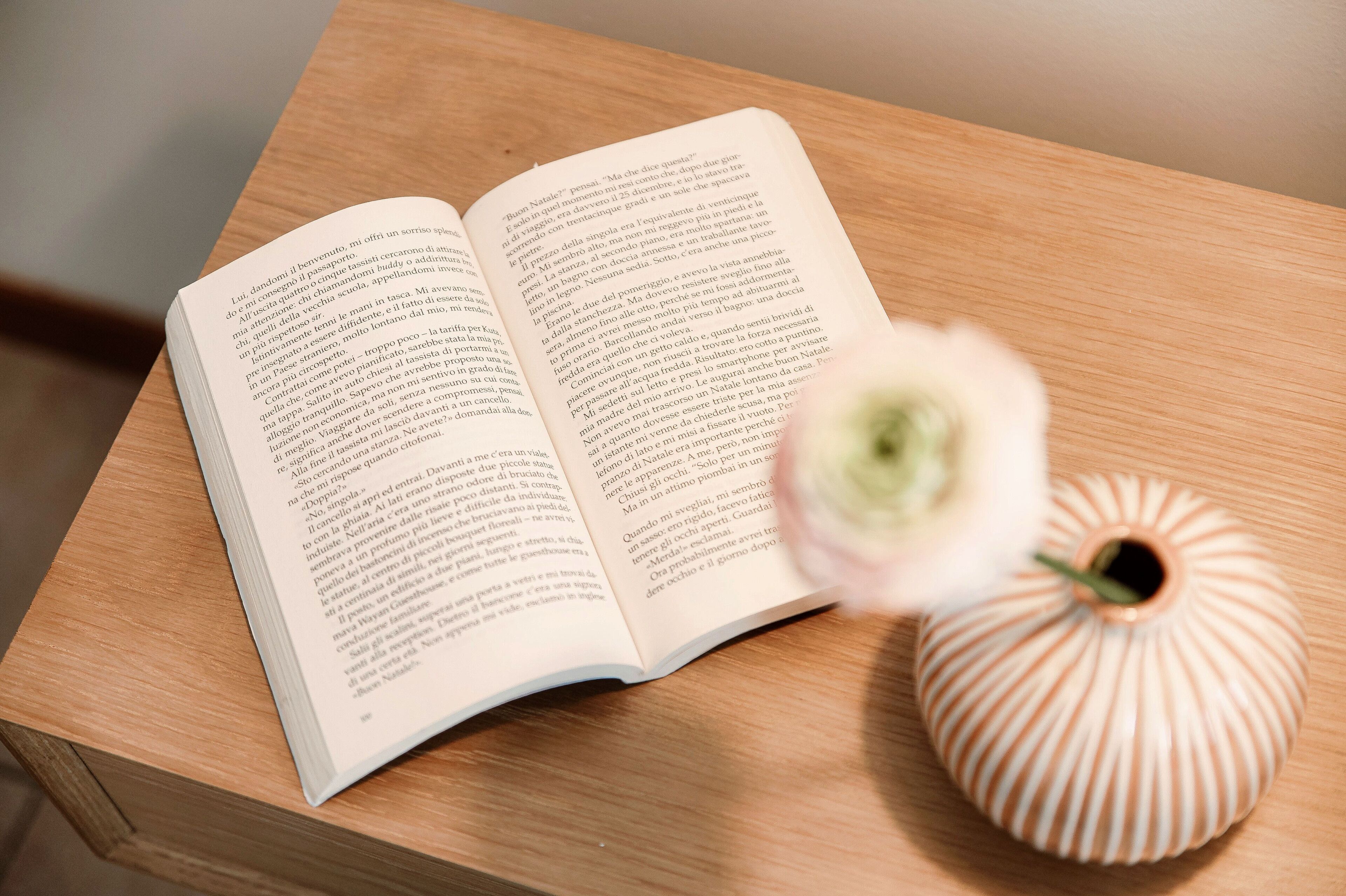 Un libro abierto sobre una mesa de madera con un jarrón blanco.