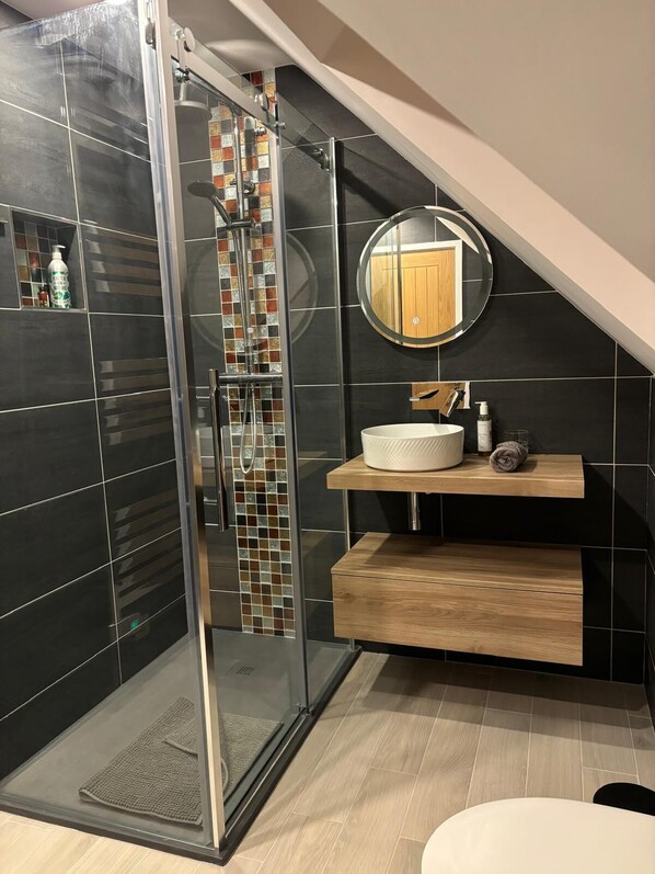 Un baño moderno con ducha envuelta en vidrio, un espejo redondo y un tocador de madera.