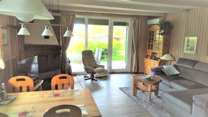 A living room with a sofa, a wooden table, a chair, and a television. There is a sliding glass door leading to an outdoor area. - Cozy log cabin for up to 4 people, free WLAN, fenced property (Damp)
