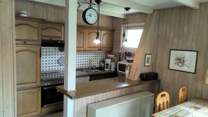 A compact kitchen with wooden cabinets, a sink, a stove, a microwave, and a clock. - Cozy log cabin for up to 4 people, free WLAN, fenced property (Damp)