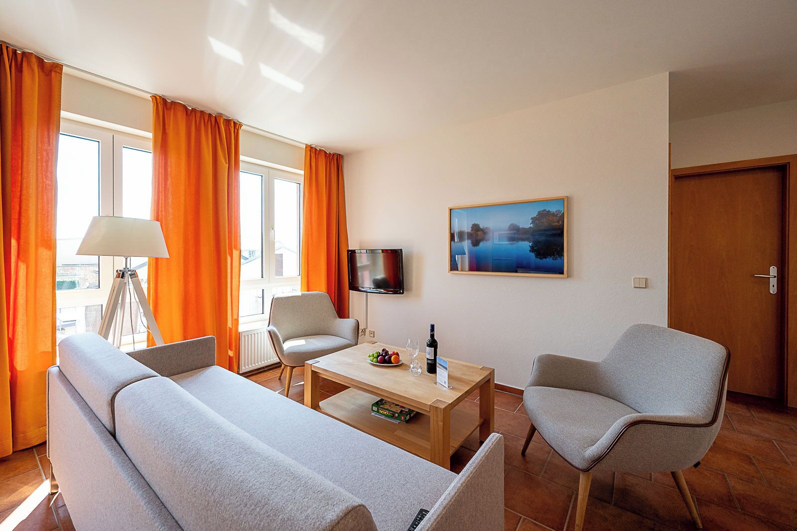 A hotel room with a sofa, two armchairs, a coffee table, a TV, and a painting on the wall.