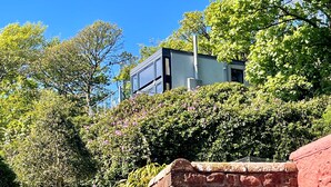 A modern building with a flat roof, surrounded by lush greenery and trees. - Cliff Top - Bubbling Springs - spectacular sea views. Sleeps 4 guests (Wemyss Bay)