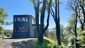 A modern two-story building with large windows, surrounded by trees and a clear view of the mountains. - Cliff Top - Bubbling Springs - spectacular sea views. Sleeps 4 guests (Wemyss Bay)