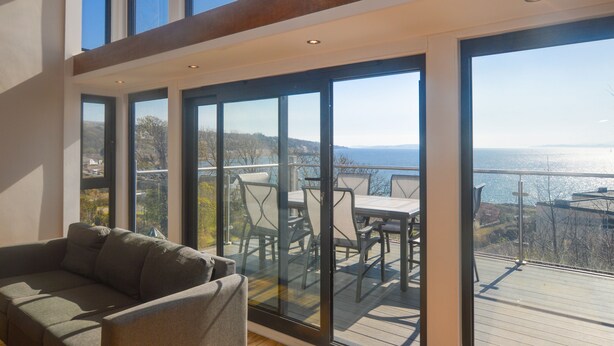 A modern interior with a glass door leading to a balcony overlooking a scenic view. - Cliff Top - Bubbling Springs - spectacular sea views. Sleeps 4 guests (Wemyss Bay)