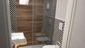 A compact bathroom with a glass-enclosed shower, a wooden vanity, and a white toilet. - Dimora Neapolis (Naples)