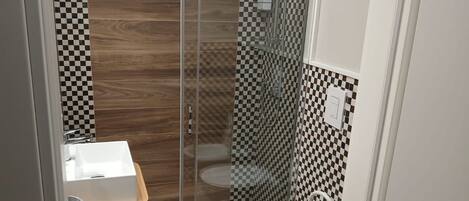 A compact bathroom with a glass-enclosed shower, a wooden vanity, and a white toilet.
