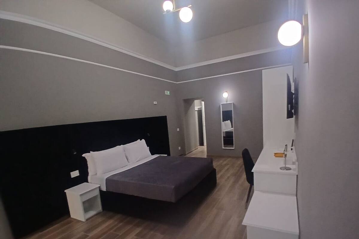 A modern hotel room with a large bed, bedside tables, a desk, and a mirror.