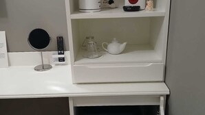 A white shelf with a coffee maker, a teapot, and a glass carafe. Below the shelf, there's a small, dark-colored cabinet with a blue light. - Dimora Neapolis (Naples)