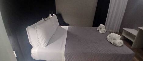 A hotel room with a bed, pillows, a bedside table, and a small table with towels.
