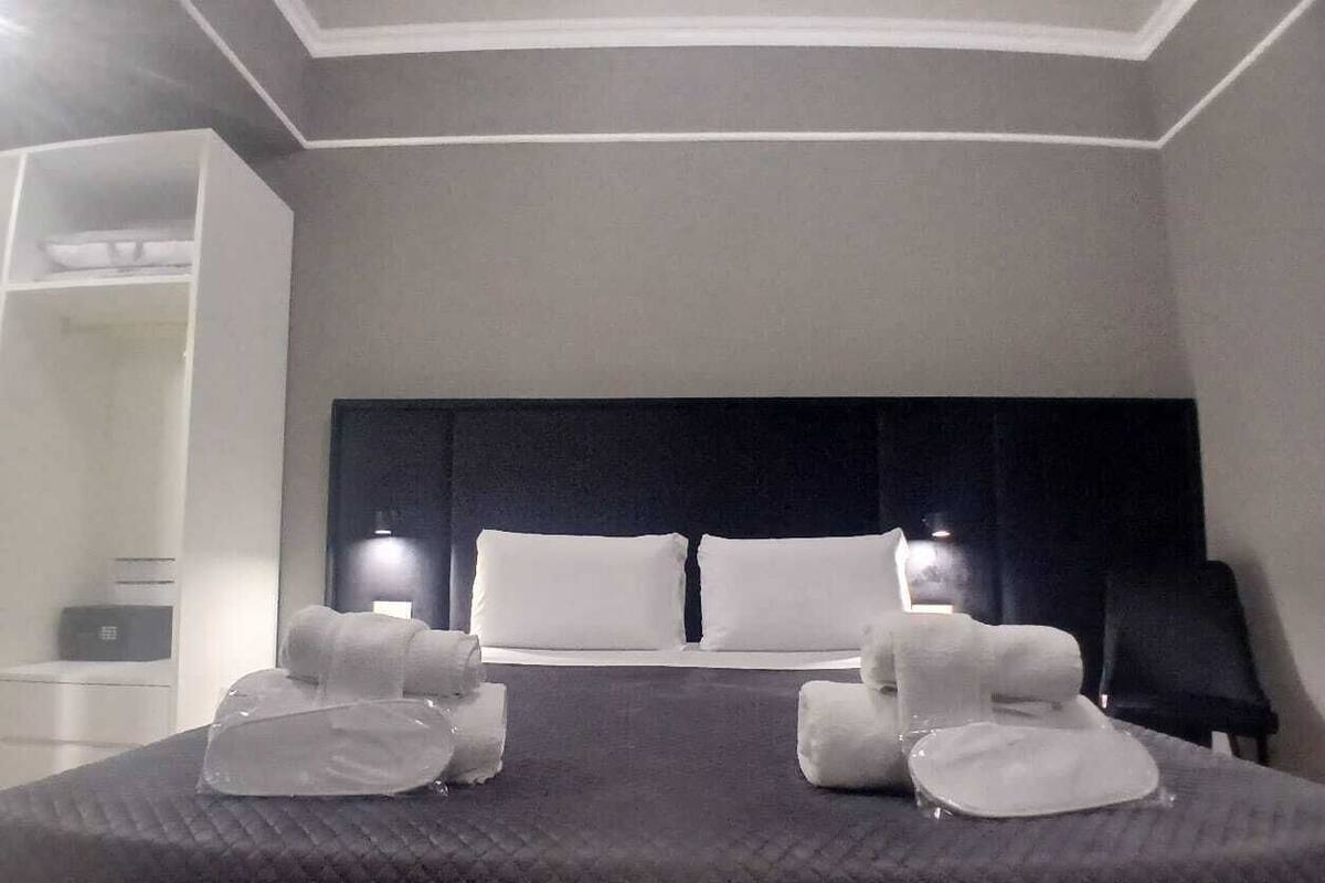 A hotel room with a large bed, two bedside lamps, a headboard, and a wardrobe.