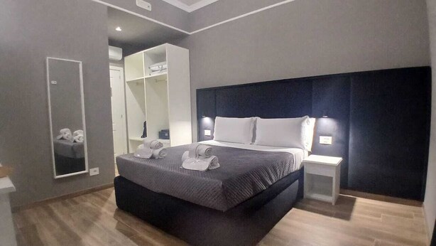 A modern hotel room with a large bed, a bedside table, a wardrobe, and a mirror. - Dimora Neapolis (Naples)