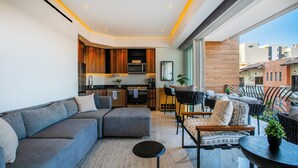 A modern living space with a grey sofa, a small round table, and a kitchen area with wooden cabinets and a microwave. - Rooftop Pool + Gym | Romantic Zone Gem (Puerto Vallarta)