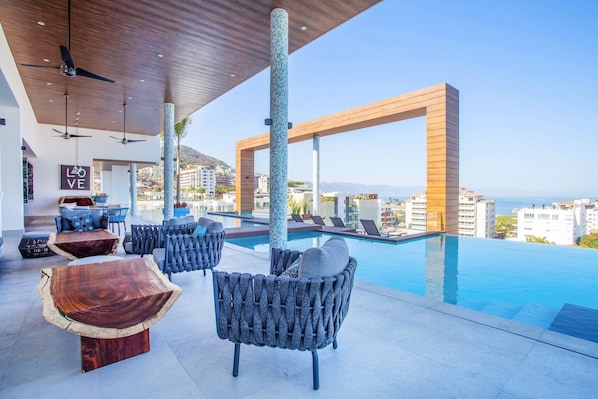 A modern outdoor lounge area with a pool, seating, and a view of the city. - Rooftop Pool + Gym | Romantic Zone Gem (Puerto Vallarta)