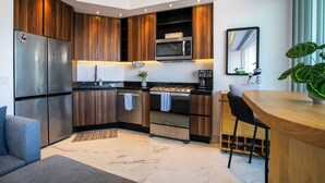 A modern kitchen with wooden cabinets, stainless steel appliances, a built-in oven, and a bar area with a chair. - Rooftop Pool + Gym | Romantic Zone Gem (Puerto Vallarta)