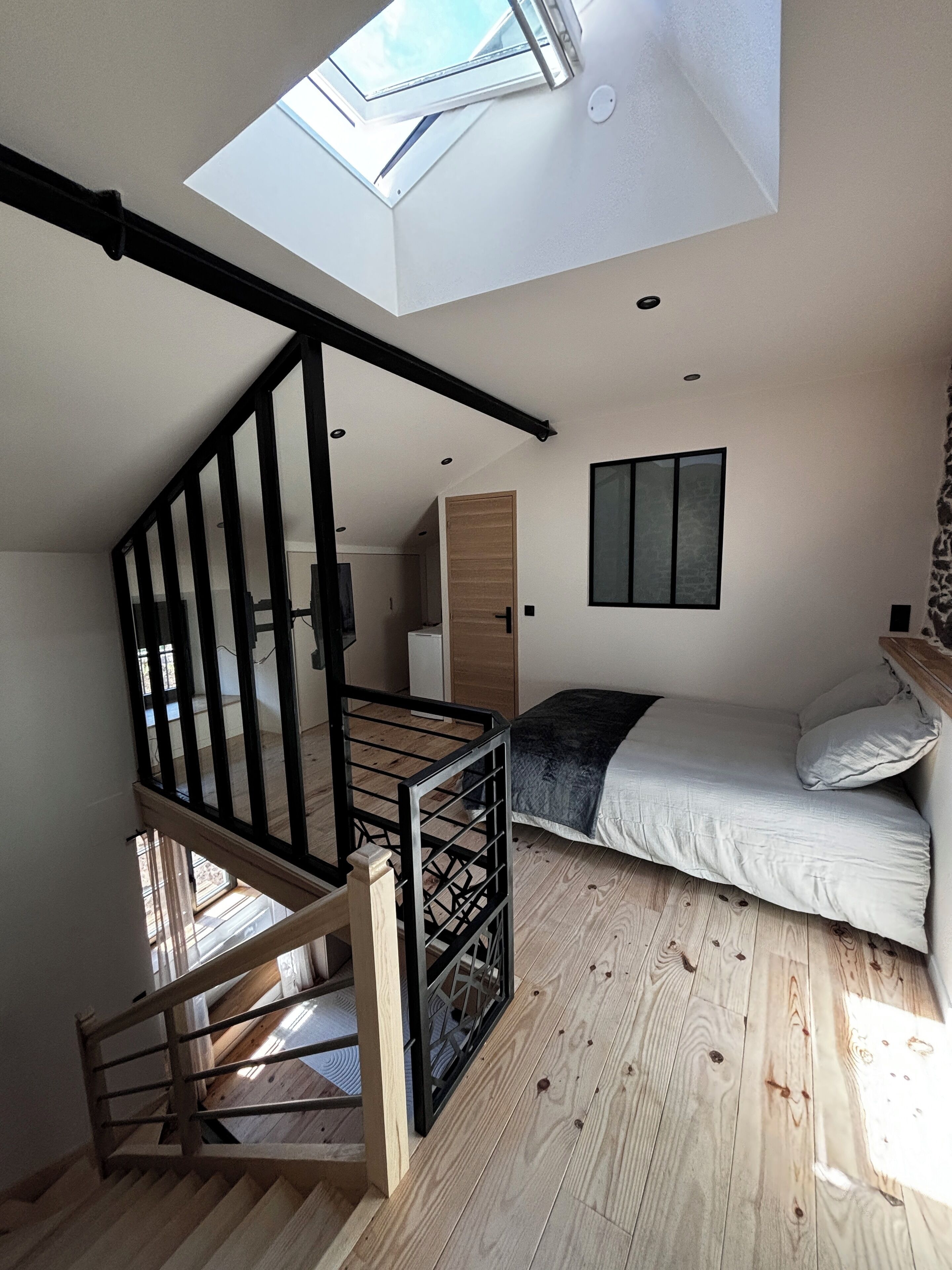 Ein Schlafzimmer im Loft-Stil mit Dachfenster, einer Holztreppe und einem Bett mit Kissen.