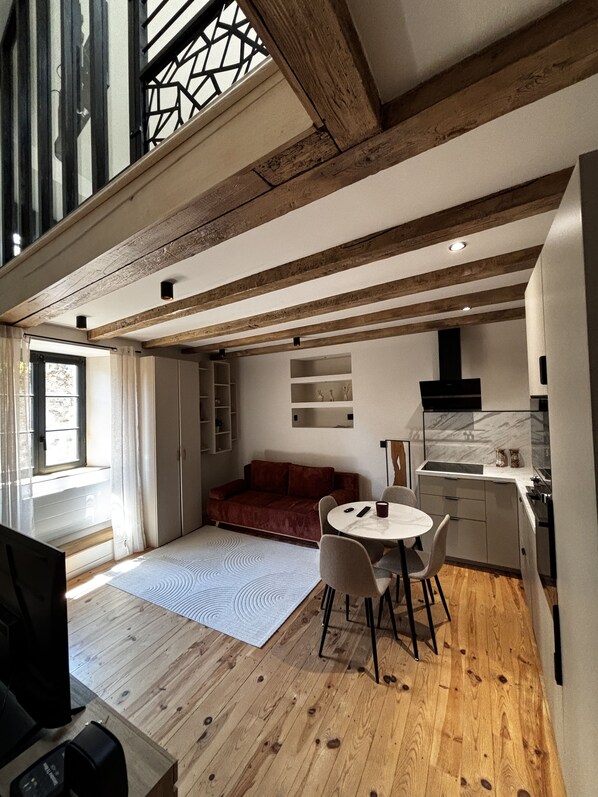 A modern kitchen with a marble backsplash, wooden beams, and a dining area with a round table and chairs. - Cosy Duplex - Equipped & Central (Saint-Flour)