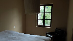 Une chambre à coucher avec un grand lit, une fenêtre, une chaise et un luminaire suspendu.
